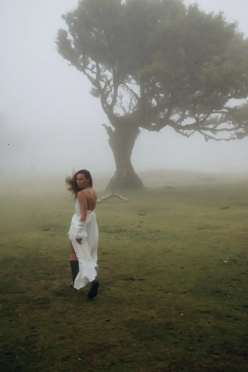 A woman in a white dress under a laurel tree in the Fanal fog