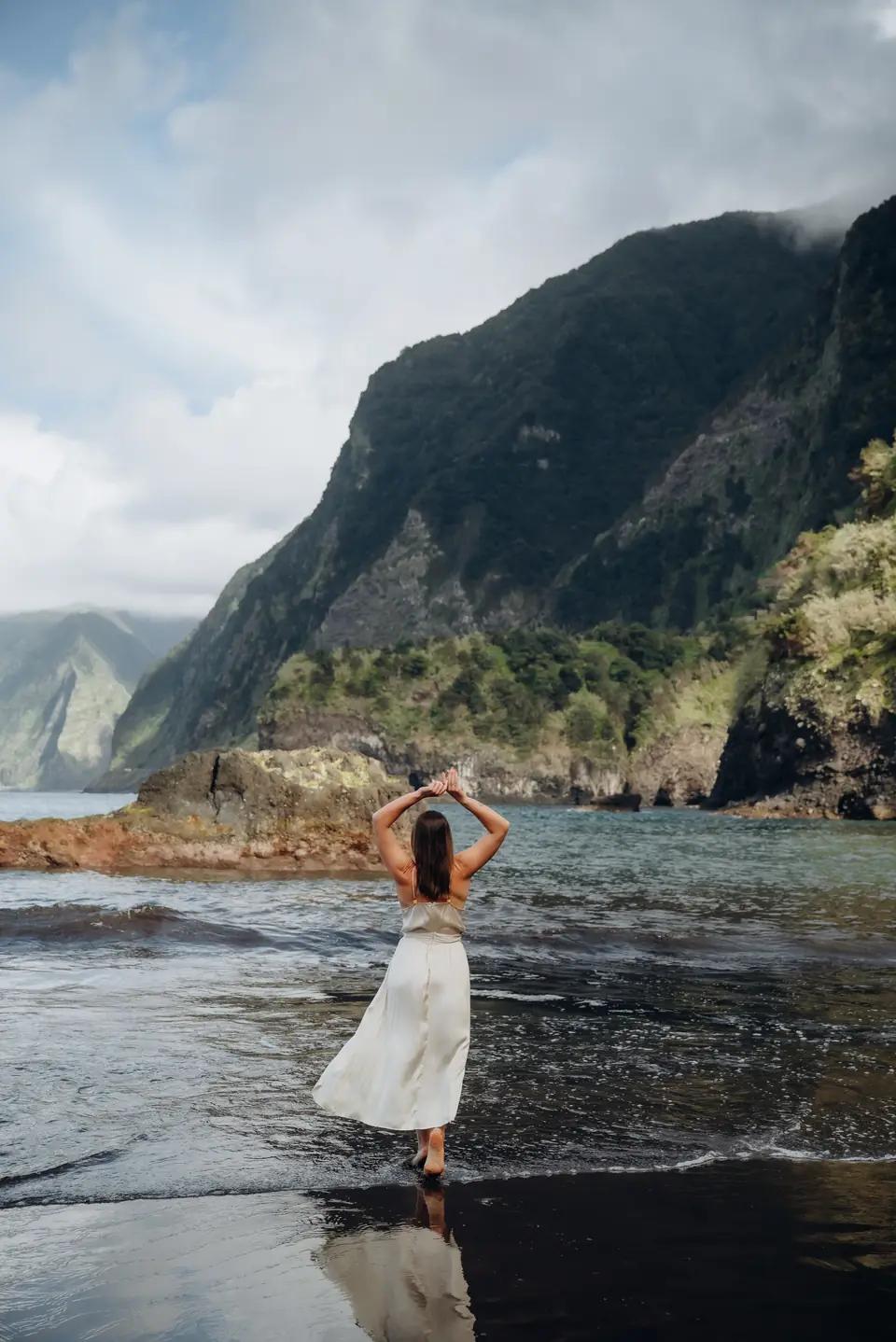 A woman in a white dress on a black-sand beach in the north of Madeira